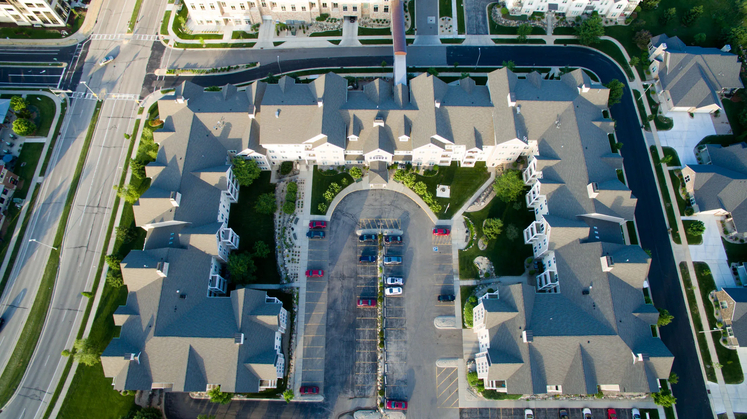 Aerial view of a large residential apartment complex with a central parking lot surrounded by green lawns and trees.